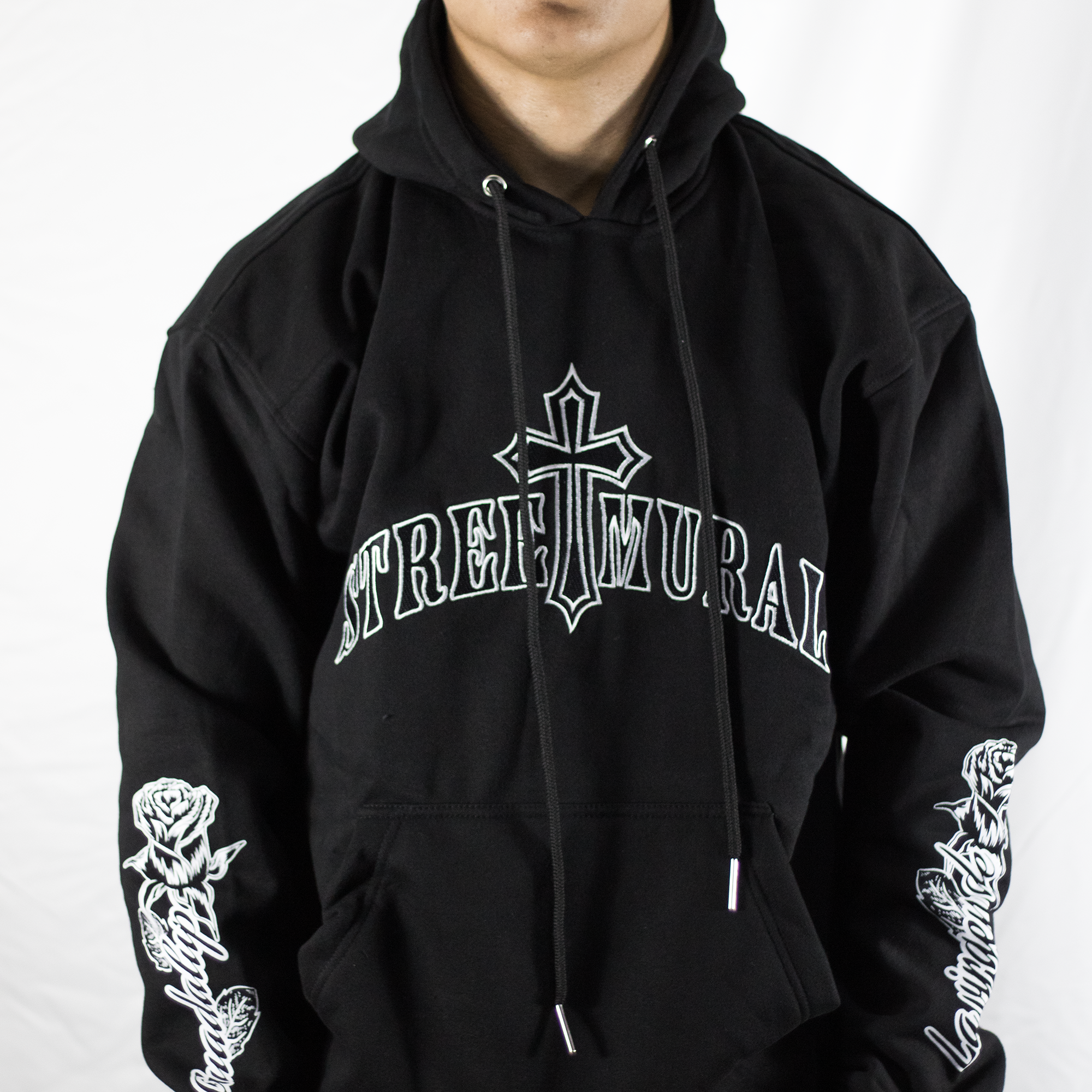 Person wearing a black hoodie with 'Street Mural' logo and rose designs on sleeves against a white background